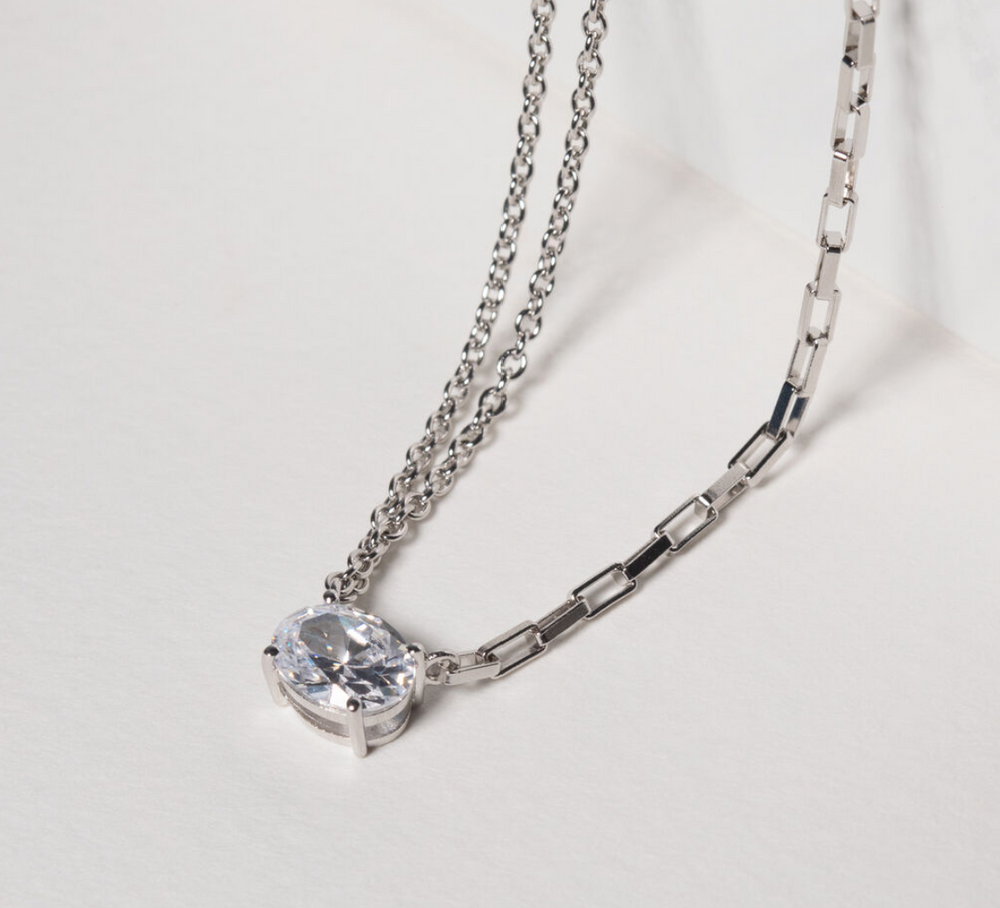 Necklace made of 925 Sterling Silver with rhodium, polished surface, and handset with facet cut white zirconia. on a table